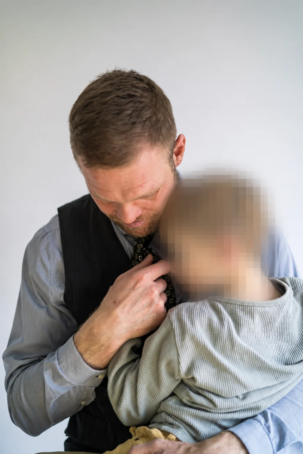Daniel Lenz hält seinen Sohn nah im Arm; der Kopf seines Sohnes ist zum Schutz seiner Identität unkenntlich gemacht