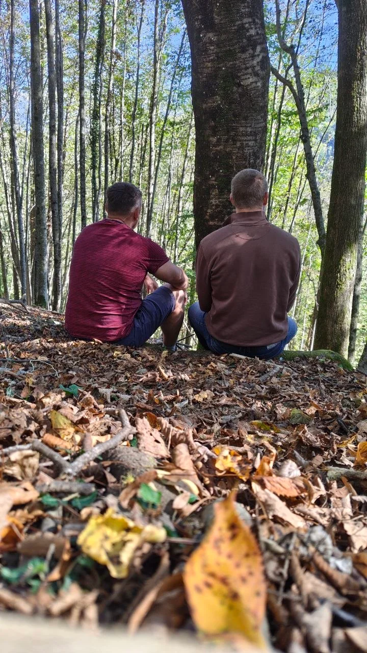 Zwei Männer sitzen nebeneinander im Wald während des ersten Slowenien-Retreats.